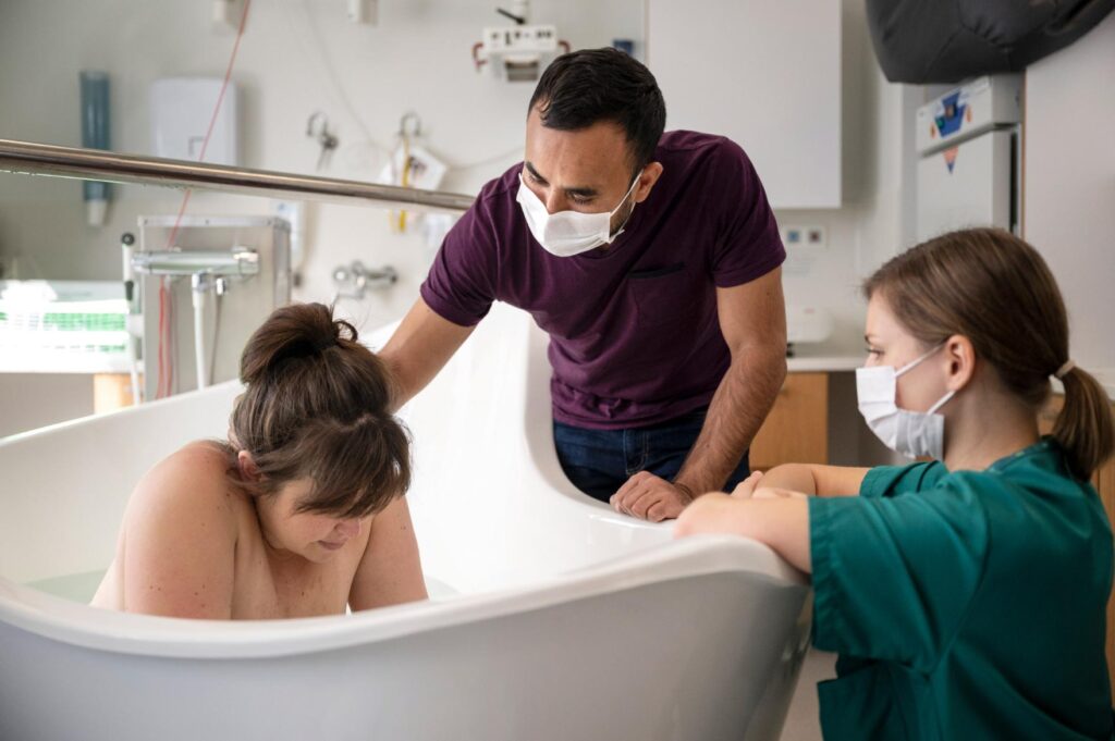 birthing person in a birthing pool with partner and midwife supporting them in birth hospital lohja 